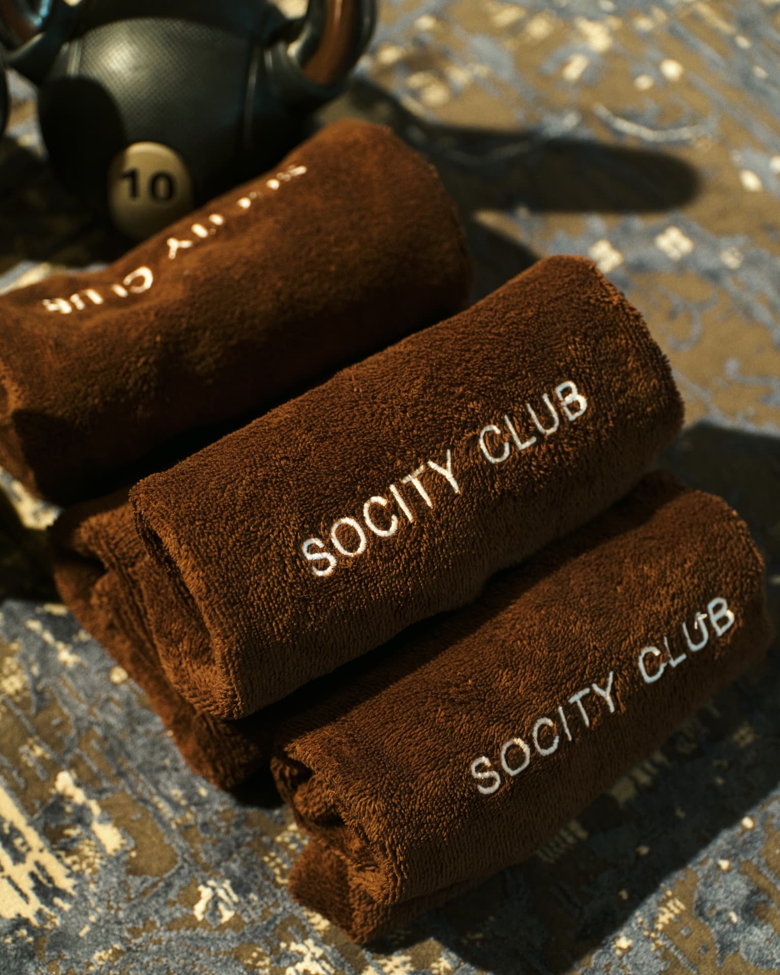 Rolled Socity Club towels beside a kettlebell in afternoon light